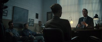 Movie still from “The Locksmith” (2023), directed by Nicolas Harvard – A woman sitting on a chair in a room; Wide shot, Over the shoulder angle