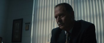 Movie still from “The Locksmith” (2023), directed by Nicolas Harvard – A man in a suit and tie sitting in front of a window; Close Up shot, Low angle