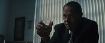 Movie still from “The Locksmith” (2023), directed by Nicolas Harvard – A man in a suit and tie holding a glass of water; Close Up shot, Low angle