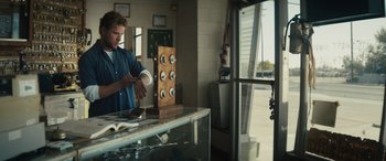 Movie still from “The Locksmith” (2023), directed by Nicolas Harvard – A man standing in front of a counter holding a coffee cup; Medium shot, Over the shoulder angle
