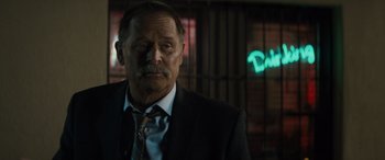 Movie still from “The Locksmith” (2023), directed by Nicolas Harvard – A man in a suit and tie standing in front of a neon sign; Close Up shot, Over the shoulder angle