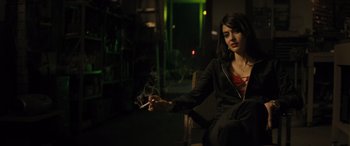 Movie still from “The Locksmith” (2023), directed by Nicolas Harvard – A woman sitting in a chair holding a cigarette in her hand; Medium shot, Low angle