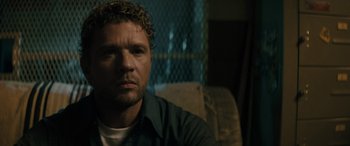 Movie still from “The Locksmith” (2023), directed by Nicolas Harvard – A person sitting on a couch; Close Up shot, Over the shoulder angle