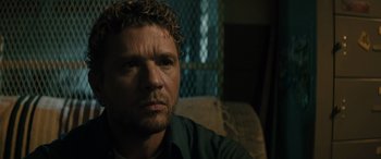 Movie still from “The Locksmith” (2023), directed by Nicolas Harvard – A person sitting on a couch; Close Up shot, Over the shoulder angle