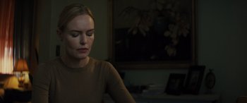 Movie still from “The Locksmith” (2023), directed by Nicolas Harvard – A woman sitting in front of a painting in a dark room; Close Up shot, Over the shoulder angle