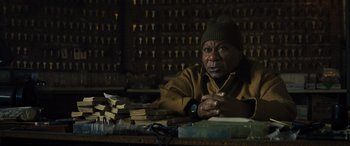 Movie still from “The Locksmith” (2023), directed by Nicolas Harvard – A man sitting in front of a pile of books; Close Up shot, High angle