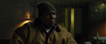 Movie still from “The Locksmith” (2023), directed by Nicolas Harvard – A man wearing a brown jacket and a green hat; Close Up shot, Low angle