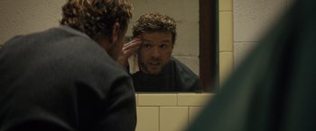 Movie still from “The Locksmith” (2023), directed by Nicolas Harvard – A man looking in the mirror in front of a bathroom mirror; Close Up shot, Over the shoulder angle