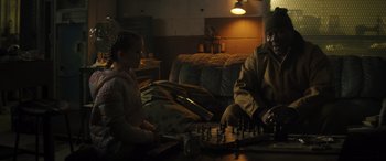 Movie still from “The Locksmith” (2023), directed by Nicolas Harvard – A man and a woman playing a game of chess in a living room; Medium shot, Over the shoulder angle