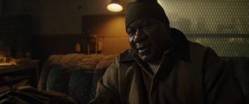 Movie still from “The Locksmith” (2023), directed by Nicolas Harvard – An older man wearing a brown jacket and a green hat; Close Up shot, High angle