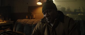 Movie still from “The Locksmith” (2023), directed by Nicolas Harvard – A person sitting in a room; Close Up shot, Over the shoulder angle