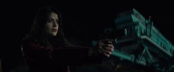 Movie still from “The Locksmith” (2023), directed by Nicolas Harvard – A woman is holding a gun in a dark room; Close Up shot, Low angle
