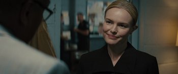 Movie still from “The Locksmith” (2023), directed by Nicolas Harvard – A woman in a black dress smiling for the camera; Close Up shot, Over the shoulder angle