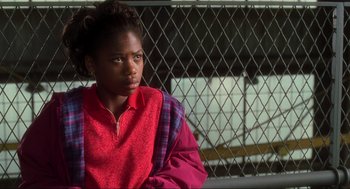 Movie still from “The Lost World: Jurassic Park” (1997), directed by Steven Spielberg – A young black woman sitting in front of a chain link fence; Close Up shot, High angle