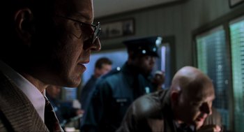 Movie still from “The Lost World: Jurassic Park” (1997), directed by Steven Spielberg – A group of people in a room with a man in glasses looking at something; Close Up shot, Low angle