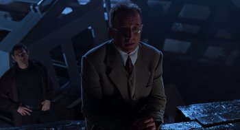 Movie still from “The Lost World: Jurassic Park” (1997), directed by Steven Spielberg – A man in a suit and tie sitting in a dark room; Medium shot, Low angle