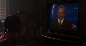 Movie still from “The Lost World: Jurassic Park” (1997), directed by Steven Spielberg – A man in a suit and red tie on a television screen; Close Up shot, Over the shoulder angle