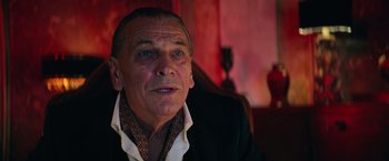 Movie still from “The Machine” (2023), directed by Peter Atencio – An older man sitting in front of a red wall; Close Up shot, Low angle