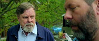Movie still from “The Machine” (2023), directed by Peter Atencio – An older man with a goatee and a beard is talking on a cell phone; Close Up shot, Over the shoulder angle