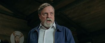 Movie still from “The Machine” (2023), directed by Peter Atencio – An older man wearing a blue jacket and white shirt; Close Up shot, Low angle