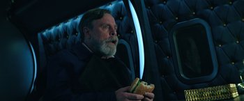 Movie still from “The Machine” (2023), directed by Peter Atencio – A man holding a sandwich while sitting in a chair; Close Up shot, Over the shoulder angle
