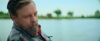 Movie still from “The Machine” (2023), directed by Peter Atencio – A man with a long beard and a plaid shirt; Close Up shot, Over the shoulder angle