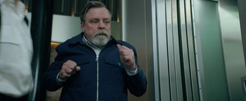 Movie still from “The Machine” (2023), directed by Peter Atencio – An older man with a goatee and a blue jacket; Medium shot, Low angle