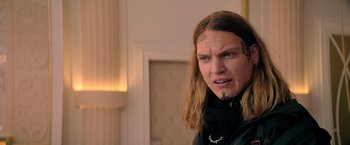 Movie still from “The Machine” (2023), directed by Peter Atencio – A man with long blonde hair and tattoos on his head; Close Up shot, Low angle