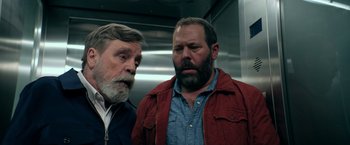 Movie still from “The Machine” (2023), directed by Peter Atencio – Two men standing next to each other in a elevator; Medium shot, Low angle