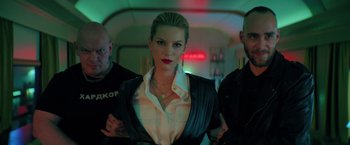Movie still from “The Machine” (2023), directed by Peter Atencio – A woman standing next to two men in a dark room; Medium shot, Low angle
