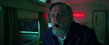 Movie still from “The Machine” (2023), directed by Peter Atencio – An older man with a beard and a surprised look; Close Up shot, Low angle