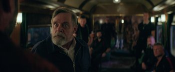 Movie still from “The Machine” (2023), directed by Peter Atencio – An old man with a beard and a mustache is sitting on a train; Close Up shot, Over the shoulder angle