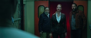 Movie still from “The Machine” (2023), directed by Peter Atencio – A man and a woman standing next to each other in front of a door; Medium shot, Low angle