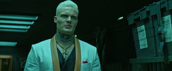 Movie still from “The Machine” (2023), directed by Peter Atencio – A man in a white suit with a cross on his neck; Close Up shot, Low angle