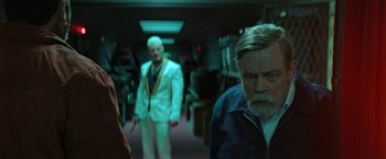 Movie still from “The Machine” (2023), directed by Peter Atencio – A man standing in front of another man holding a knife; Medium shot, Over the shoulder angle