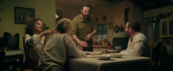 Movie still from “The Machine” (2023), directed by Peter Atencio – A man and a woman are standing at a dinner table; Medium shot, Over the shoulder angle