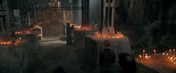 Movie still from “The Machine” (2023), directed by Peter Atencio – A person lighting candles in a church; Wide shot, High angle