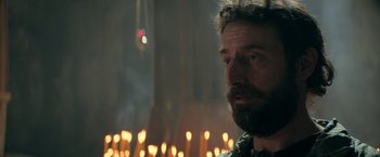 Movie still from “The Machine” (2023), directed by Peter Atencio – A man with a long beard is standing in front of candles; Close Up shot, Low angle
