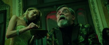 Movie still from “The Machine” (2023), directed by Peter Atencio – An old man with a beard and a woman in the background; Medium shot, Low angle