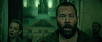 Movie still from “The Machine” (2023), directed by Peter Atencio – A man with a goatee and a beard stares at the camera; Close Up shot, Low angle