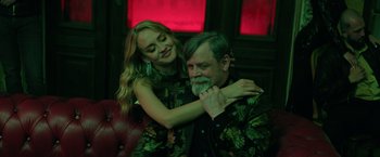 Movie still from “The Machine” (2023), directed by Peter Atencio – A woman hugging a man in front of a red wall; Medium shot, Over the shoulder angle