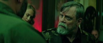 Movie still from “The Machine” (2023), directed by Peter Atencio – An older man with long grey hair and a beard; Close Up shot, Over the shoulder angle