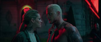 Movie still from “The Machine” (2023), directed by Peter Atencio – A man and a woman standing next to each other in front of a building; Close Up shot, Over the shoulder angle