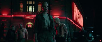 Movie still from “The Machine” (2023), directed by Peter Atencio – A man and a woman standing next to each other in front of a building; Medium shot, Low angle