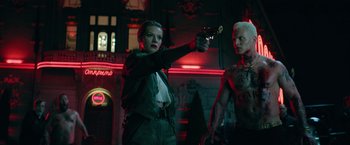Movie still from “The Machine” (2023), directed by Peter Atencio – A man and a woman holding guns in a room; Medium shot, Over the shoulder angle