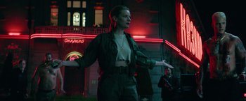 Movie still from “The Machine” (2023), directed by Peter Atencio – A woman standing in front of a building at night; Medium shot, Low angle