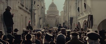 Movie still from “The Mad Women's Ball” (2021), directed by Mélanie Laurent – A crowd of people walking down a street with umbrellas; Extreme Wide shot, High angle