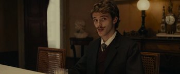 Movie still from “The Mad Women's Ball” (2021), directed by Mélanie Laurent – A man in a suit sitting at a dinner table; Close Up shot, Low angle