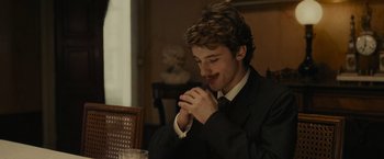 Movie still from “The Mad Women's Ball” (2021), directed by Mélanie Laurent – A man in a black suit and a white shirt is sitting at a table; Close Up shot, Over the shoulder angle