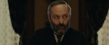 Movie still from “The Mad Women's Ball” (2021), directed by Mélanie Laurent – An old man with a beard and a mustache; Close Up shot, Over the shoulder angle